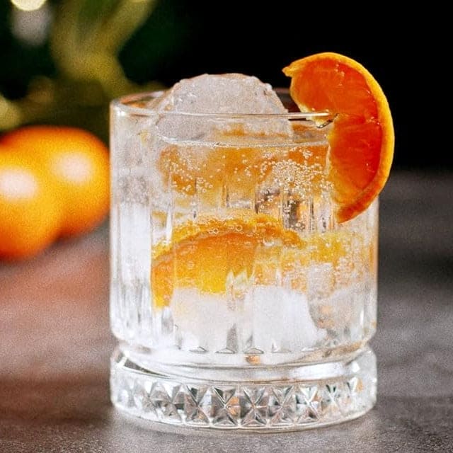 Glass of Clementine Gingerbread Christmas liqueur with ice and orange slice garnish